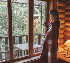 cozy window treatments to elevate your space this fall, Woman in a blanket looking out of a window image via Canva